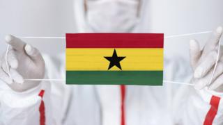 A person holding a face mask with the Ghanaian flag on it