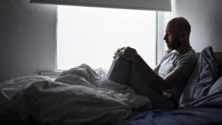 hombre en su cama mira hacia la ventana