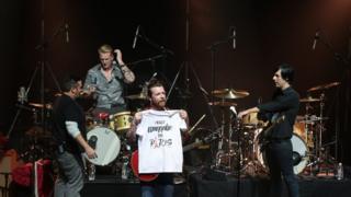イーグルス・オブ・デス・メタルがパリ・オランピア劇場で演奏。ジェシー・ヒューズ(中央)が「本当にパリにいきたい」と書かれたTシャツを広げて見せた(16日)