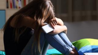 Teenager holding a mobile phone sitting on his bed