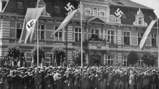 Multidão diante de edifício público em Demmin, decorado com bandeiras nazistas em 1936