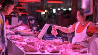 Покупатель (L) покупает мясо на рынке в Шэньяне в северо-восточной китайской провинции Ляонин 12 июня 2019 г.
