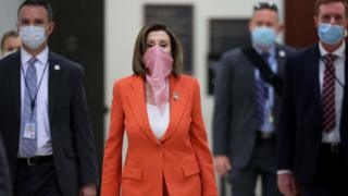 Спикер палаты представителей Нэнси Пелоси (штат Калифорния) в шарфе, закрывающем рот и нос, окружена охраной и персоналом, когда она прибывает на свою еженедельную пресс-конференцию во время новой пандемии коронавируса в Капитолии США 24 апреля 2020 года в Вашингтоне. DC