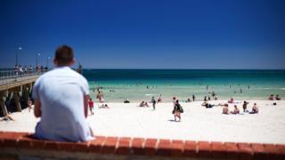 Люди наслаждаются пляжем Аделаиды Гленелг среди жары в начале месяца