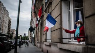 Woman waving French flag out of window with coronavirus mask on in a Parisian suburb