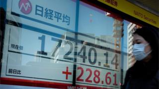 A pedestrian walks in front of a quotation board displaying the share price numbers of the Tokyo Stock Exchange in Tokyo (March 18, 2020).