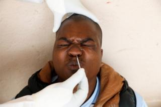 A man clamps his eyes and mouth shut as a swab is inserted into his nose.