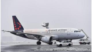 A Brussels airlines plane is seen on a snowy runway with vehicles de-icing it in this file photo