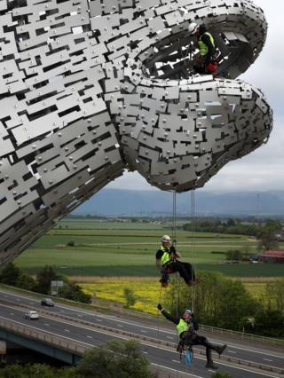 Men suspended from the Kelpies on wires