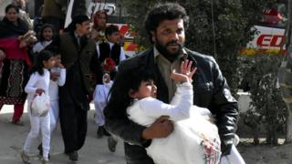 A bearded man carries a girl, dressed in white, from the scene of the attack