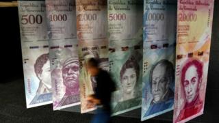 Un hombre pasa delante de unos carteles de los billetes venezolanos.