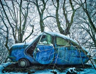 An abandoned blue car in an icy forest