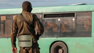 A service member of pro-Russian troops stands guard on a road near a bus carrying Ukrainian soldiers, who surrendered at the besieged Azovstal steel mill in the course of Ukraine-Russia conflict, near Mariupol, Ukraine