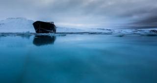 A small boat in blue water with mountains behind. Photograph by Clare Kines