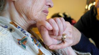 Elderly person holding hands with a carer