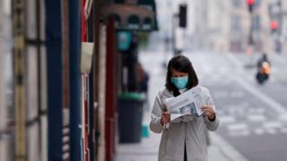 Женщина в защитной маске читает газету, идя по улице на заброшенном острове Сен-Луи в Париже