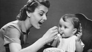 Imagen en blanco y negro de madre dándole de comer a hijo.