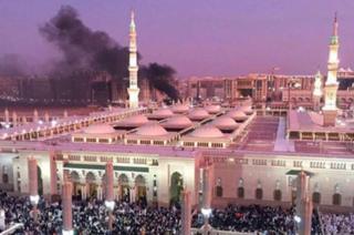 black smoke billowing from behind a huge mosque with many people outside