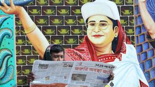 বাংলাদেশী পাঠক তৎকালীন বিরোধী নেতা শেখ হাসিনার পোস্টারের সামনে জরুরী অবস্থার খবর জানছেন, ১২-০১-২০০৭।