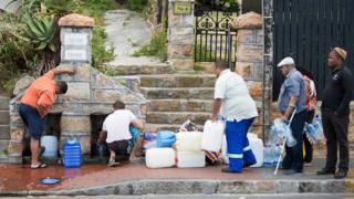 Люди собирают питьевую воду из труб, питаемых подземным источником, в Сент-Джеймсе, примерно в 25 км от центра города, 19 января 2018 года в Кейптауне.