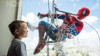 A child smiles as 'Spiderman' scrubs the window from the other side