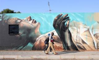 A couple walk past an art work by German artist @norm_abartig and South African artist @dekor as part of the Westdene Graffiti Project in downtown Johannesburg, South Africa, 09 October 2018.