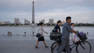 Pyongyangites go about their daily business with the Tower of Juche in the background