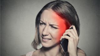 Chica usando celular con dolor de cabeza.