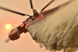 A helicopter drops fire retardant on the ground