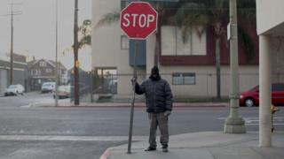 Home na rua, segurando placa de trânsito, em Skid Row, Los Angeles