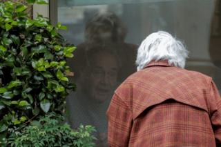 in_pictures An elderly man and woman talk to each through a closed window