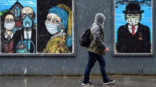 pedestrian-walks-past-paintings-wearing-masks-in-glasgow