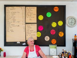 Babs sat under the menu board in BABS cafe. Blyth, Nottinghamshire.