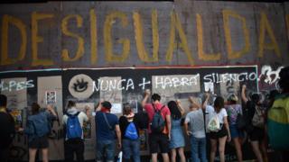 People demonstrate under graffiti reading "Inequality" during a protest demanding greater social reforms from Chilean President Sebastian Pinera in Santiago on 12 November, 2019.