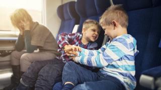 Una mujer en un tren con dos niños traviesos al lado