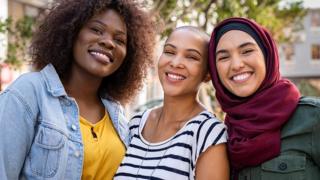 Group of three happy multiethnic friends looking at camera.