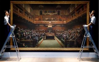 Gallery assistants pose with an artwork entitled Devolved Parliament by British artist Banksy