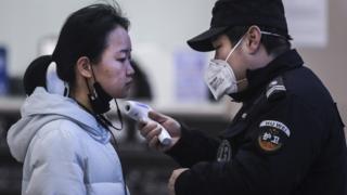 Mulher tem a temperatura medida em checagem feita em Wuhan, na China