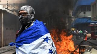 A student of the National Autonomous University of Honduras (UNAH) wrapped in a Honduran national flag is seen next to a fire that blocks a road during a protest against the approval of education and healthcare bills in the Honduran Congress in Tegucigalpa on April 29, 2019