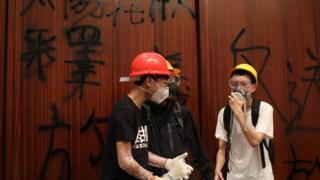 Protesters stand by a wall covered in graffiti