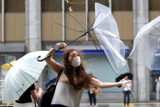 A woman using an umbrella struggles against heavy rain and wind