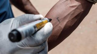 A Red Cross volunteer marks a person's arm with a tick at Nakasero market in Kampala, Uganda - Wednesday 1 April 2020