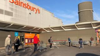 Shoppers observe social distancing as they queue outside Sainsbury's