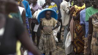 An African child standing among adults and looking into the camera