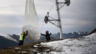 Two men help a helicopter carrying snow near Luchon in French Pyrenees