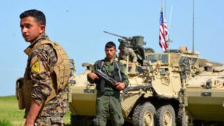 Kurdish fighters stand beside US military vehicles in the town of Darbasiya next to the Turkish border, Syria (29 April 2017)