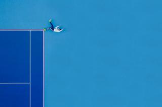 A person poses on the ground at a tennis court.