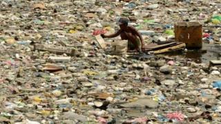 A scavenger wades through garbage in Manila, 2016