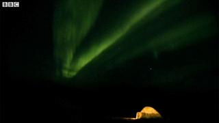 Un domo iluminado en medio de una oscuridad alumbrada por las luces de la aurora boreal.