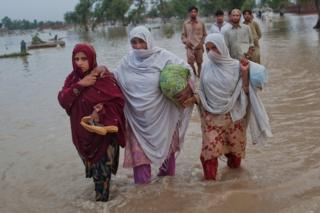 Три женщины в Пакистане пробираются сквозь паводковые воды, неся свои вещи